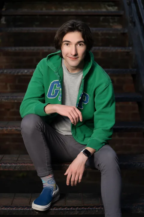 Cade in a green hoodie sitting on outdoor stairs